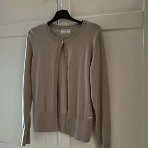 Beige kofta från Lindex - Elegant beige kofta från holly & whyte (lindex) med rund hals och knappar framtill. Perfekt för en stilren look. Långärmad design med ribbade kanter för extra komfort. skriv för mer bilder 💞💞