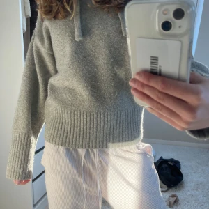 Grå stickad hoodie från Zara - Säljer en mysig grå stickad hoodie från Zara. Tröjan har långa ärmar och en ribbad nederkant samt muddar. Perfekt för kyliga dagar med sin mjuka och bekväma passform.