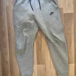 Grå mjukisbyxor från Nike - Säljer ett par grå mjukisbyxor från Nike med svart logga på sidan. Byxorna har en elastisk midja med snörning och sidofickor. Perfekta för en avslappnad stil. Helt ny knappast använt Dtorlek Xs
