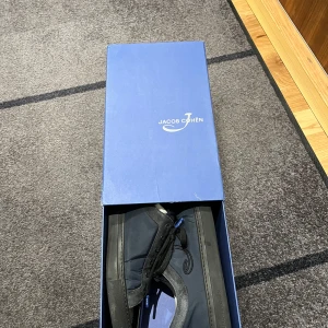 Svarta/blåa sneakers från Jacob Cohen - Snygga svarta, blåa sneakers från Jacob Cohen med glansiga detaljer på tån och snörning. Perfekta för en stilren look.  Skorna har sett lite användning men är i väldigt bra skick. Kommer med låda. Kom gärna med prisförslag