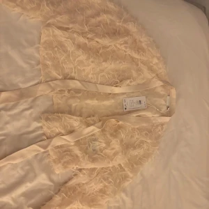 Beige cardigan jacka från Vila - helt ny!Säljer en elegant beige cardigan jacka från Vila med fjäderliknande detaljer. Jackan har långa ärmar och en öppen med rosett knytning.Perfekt för att lägga till en touch av glamour till din outfit.