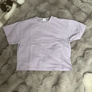 Ljuslila t-shirt från Lindex Kids - En basic ljuslila t-shirt från Lindex Kids i mjuk bomull. Modellen är rak med korta ärmar och rund halsringning. Perfekt för en enkel och stilren look.