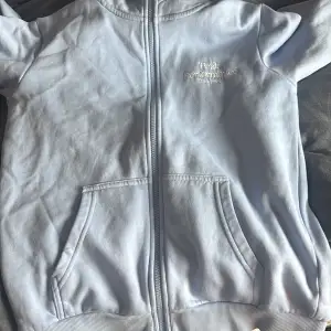 Säljer en ljusblå hoodie från Peak Performance med dragkedja framtill och två fickor. Tröjan har huva och broderad logga på bröstet. Perfekt för en avslappnad stil och enkel att matcha med jeans eller mjukisbyxor.