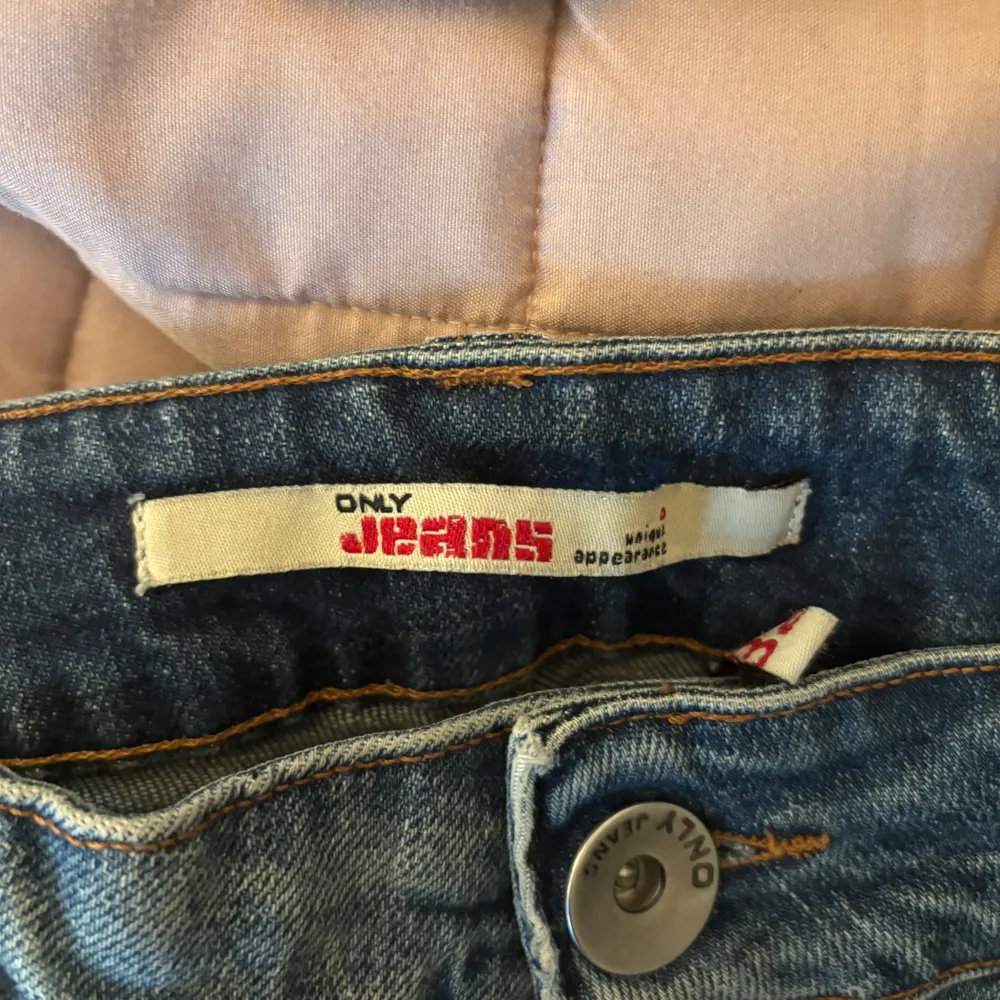 Säljer ett par klassiska blå jeansbyxor från ONLY med lätt slitna detaljer och raka ben. Byxorna har normal passform, fem fickor och stängs med dragkedja och knapp. Perfekta för en avslappnad stil.. Farkut & Housut.