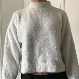 Vit fluffig stickad tröja  - Mysig vit stickad tröja och lång ärm. Tröjan har en fluffig textur och bred ribbad kant nedtill och vid ärmsluten. Perfekt för kyliga dagar.