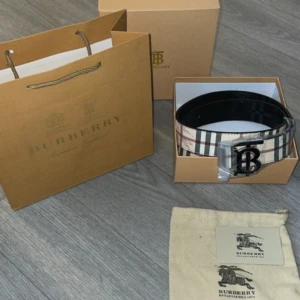 Burbbery bälte  - Säljer ett klassiskt Burberry bälte med det ikoniska rutiga mönstret i beige, svart, rött och vitt. Bältet har ett stort metallspänne med ett B framtill. Perfekt accessoar för att lyfta din outfit.