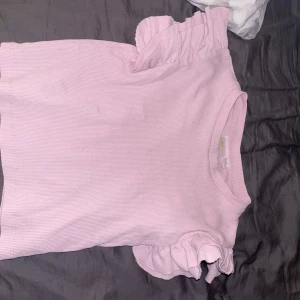Ljusrosa ribbad topp med volangärmar från Gina Tricot - Supersöt ljusrosa topp från Gina Tricot med ribbad struktur och korta ärmar med volangdetaljer. Säljer den för att den är för liten!🩷