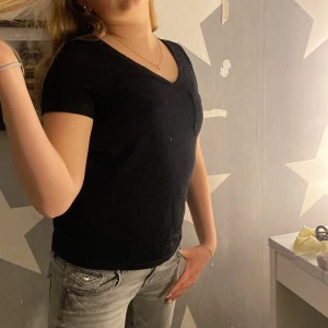 Svart t-shirt med v-ringning från Object - En svart t-shirt från Object i storlek XS. T-shirten har v-ringning, korta ärmar och en bröstficka. Perfekt basplagg i mjukt material som passar till mycket.