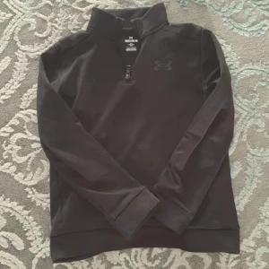 Under Armour - Säljer en svart långärmad tröja från Under Armour med halv dragkedja framtill och hög krage. Helt ny har inte använt den!!! 