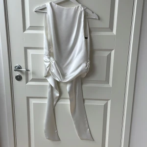 Vit satin topp från Zara - Elegant vit topp i satin från Zara med öppen rygg och band som man knyter på baksidan. Skulle säga att den är lite i de kortare designen och slutar ovanför naveln. Är knappt använd och i mycket bra skick!