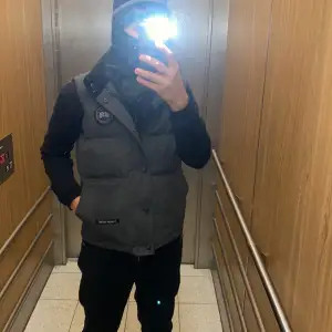 Säljer en grå dunväst från Canada Goose med klassisk logotyp på bröstet och knappar framtill. Västen har två stora fickor och är perfekt för lager-på-lager. Stilsäker och varm för kyliga dagar byte kan tas imot hör av sig vid frågor eller intresse!