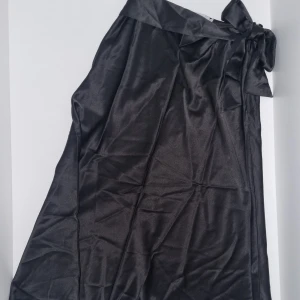 Svart satinkjol från Nicci Hernestig × NAKD - Snygg svart midi-satinkjol från Nicci Hernestig x NAKD. Kjolen har knytband i midjan och en elegant, enkel design som passar perfekt till många olika stilar. Kjolen är i storlek 34 och har en klassisk svart färg. Tveka inte att höra av för bättre bilder!