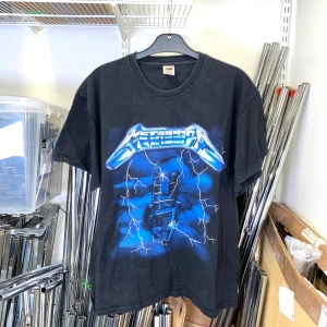 Svart t-shirt med Metallica-tryck  - Svart t-shirt med Metallica-tryck framtill i blått och vitt, med blixtar. Baksidan har Metallica-logga i grått. Klassisk passform och rund hals.  Strl: L-XL.  /  Spara skärmtid, besök våra butiker i Sthlm, Malmö & Gbg. New arrivals daily + studentrabatt i alla våra butiker! Hitta till din närmsta butik på humansecondhand.se.   HUMANA Second Hand erbjuder 14 dagars retur, även via plick. Returer skickas med PostNord. Vid retur kontakta support@plick.se.