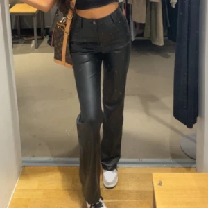 Svarta skinnbyxor med hög midja - Snygga svarta skinnbyxor med hög midja och raka ben. Byxorna har klassisk femficksdesign och stängs med knappar och dragkedja. Perfekta att styla med crop top eller oversized tröja.