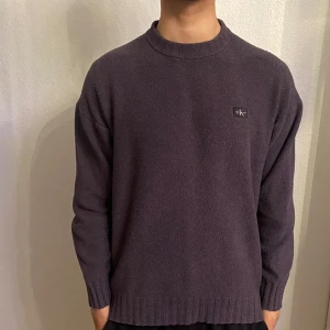 Mörklila stickad tröja från Calvin Klein Jeans - Säljer en mörklila stickad tröja från Calvin Klein Jeans. Tröjan har rund halsringning, långa ärmar och en liten logotyp på bröstet. Perfekt för dig som gillar enkel och stilren design. Oversised
