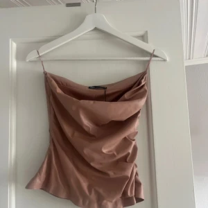 Rosa satinlinne från Zara - Säljer ett snyggt rosa satinlinne från Zara med tunna axelband och draperad halsringning. Perfekt för att lyfta vilken outfit som helst med sin glansiga finish och eleganta look.