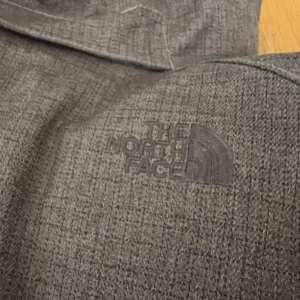 Brun vinterjacka från The North Face - Säljer en brun vinterjacka från The North Face med huva och dragkedja. Jackan har flera fickor framtill och diskret mönster i tyget. Perfekt för kalla dagar och har en sportig look.