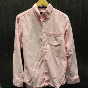Ljusrosa skjorta från GANT - Säljer en ljusrosa skjorta från GANT i klassisk oxfordstil. Skjortan har lång ärm, bröstficka med broderad logga och knappar framtill. 