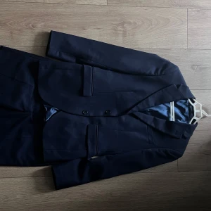 Mörkblå kostym köpt hos brothers.  - Säljer en klassisk mörkblå kostym med tvådelad design: kavaj med två knappar och matchande byxor. Kavajen har smal passform, klassiska slag och fickor med lock. Perfekt för formella tillfällen som bal eller nyår. 