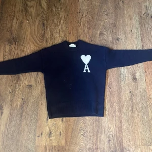 Mörkblå stickad tröja med hjärta från Ami - Säljer en mörkblå stickad tröja från Ami Alexandre Mattiussi. Tröjan har ett vitt hjärta och bokstaven A broderat på bröstet. Klassisk rund halsringning och ribbade muddar vid ärmslut och nederkant. Perfekt för en stilren look. S men passar xs