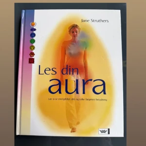 Les din aura - Boken 'Les din aura' av Jane Struthers lär dig att se energifältet runt dig och tolka färgernas betydelse. Omslaget har en bild på en person omgiven av ett färgglatt ljus och symboler längs ryggraden. Texten är på norska.