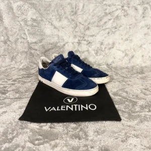 Blå och vita sneakers från Valentino - Snygga blå och vita sneakers från Valentino med en stilren design. Skorna har en klassisk snörning och är tillverkade i mocka. Perfekta för en trendig look.