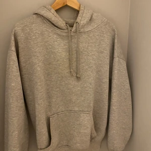 Grå hoodie från Bik Bok - Säljer en mysig grå hoodie från Bik Bok i storlek XS. Den har en klassisk design med snören i huvan och en stor magficka framtill. Perfekt för en avslappnad stil.