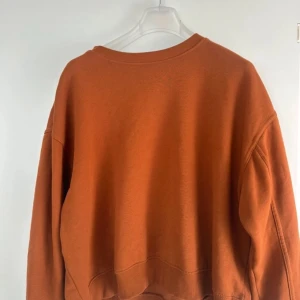 Orange sweatshirt - Säljer en snygg orange sweatshirt med rund hals och långa ärmar. Perfekt för en avslappnad stil och passar bra till jeans eller leggings. Enkelt och stilrent plagg för vardagen.
