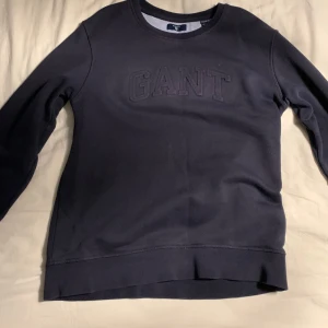 Mörkblå tröja från GANT - Säljer en stilren mörkblå tröja från GANT med broderad logga på bröstet. Tröjan har långa ärmar och en rund halsringning. Perfekt för en avslappnad och snygg look.