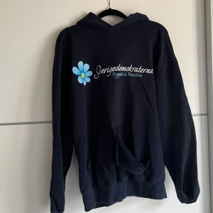 Mörkblå hoodie från Fruit of the Loom - Säljer en mörkblå hoodie från Fruit of the Loom med tryck på framsidan. Den har en klassisk design med en stor ficka framtill och en bekväm huva. Perfekt för en avslappnad stil.