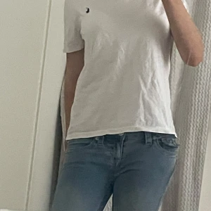Vit t-shirt från Polo Ralph Lauren - Säljer en klassisk vit t-shirt från Polo Ralph Lauren med det ikoniska broderade logotypen i marinblått på bröstet. T-shirten är kortärmad och tillverkad i mjuk bomull. Litet litet hål bak men det syns inte, kan skicka bild privat.