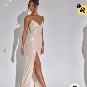 Champagnefärgad paljettklänning - Snygg champagnefärgad långklänning med paljetter och smala axelband. Klänningen har en slits framtill och en öppen rygg med snörning. Passar perfekt till balen, storleken är s-m då snörningen gör den flexibel. Klänningen är köpt för 1150 plus 500kr tull och frakt. Endast testad, lapp är kvar.