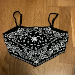 Svart bandana-mönstrad topp från Shein - Säljer en snygg svart topp från Shein med bandana-mönster i vitt. Toppen har smala axelband och en cool design som ger en unik look. Perfekt för en dag på stranden i sommar!🖤