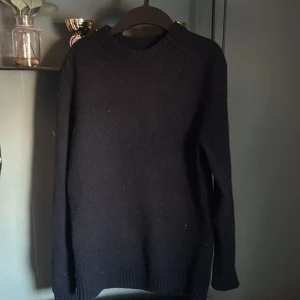 Svart tröja från East West - Säljer en stilren svart tröja från East West i mjuk lammull. Tröjan har långa ärmar och en klassisk rund halsringning. Perfekt för kyligare dagar och enkel att matcha med olika outfits.