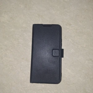 Svart mobilfodral med kortfack - Snyggt svart mobilfodral i skinn med praktiska kortfack på insidan. Fodralet har en magnetisk stängning och är designat för att skydda din telefon samtidigt som det ger enkel åtkomst till kort och ID. Perfekt för att hålla allt på ett ställe!