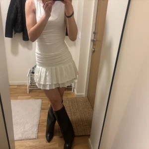 Vit ärmlös klänning med volangdetalj - Snygg vit ärmlös klänning med volangdetalj i nederkant. Perfekt för en somrig look. Klänningen har en tight passform som framhäver figuren. Funkar perfekt inför studenten 🤍🤍
