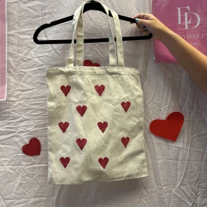 Beige shoppingväska med hjärtan - Vi är ett UF företag som säljer tygväskor med handmålade tryck på framsidan. Perfekt för att bära med sig det nödvändigaste med stil.