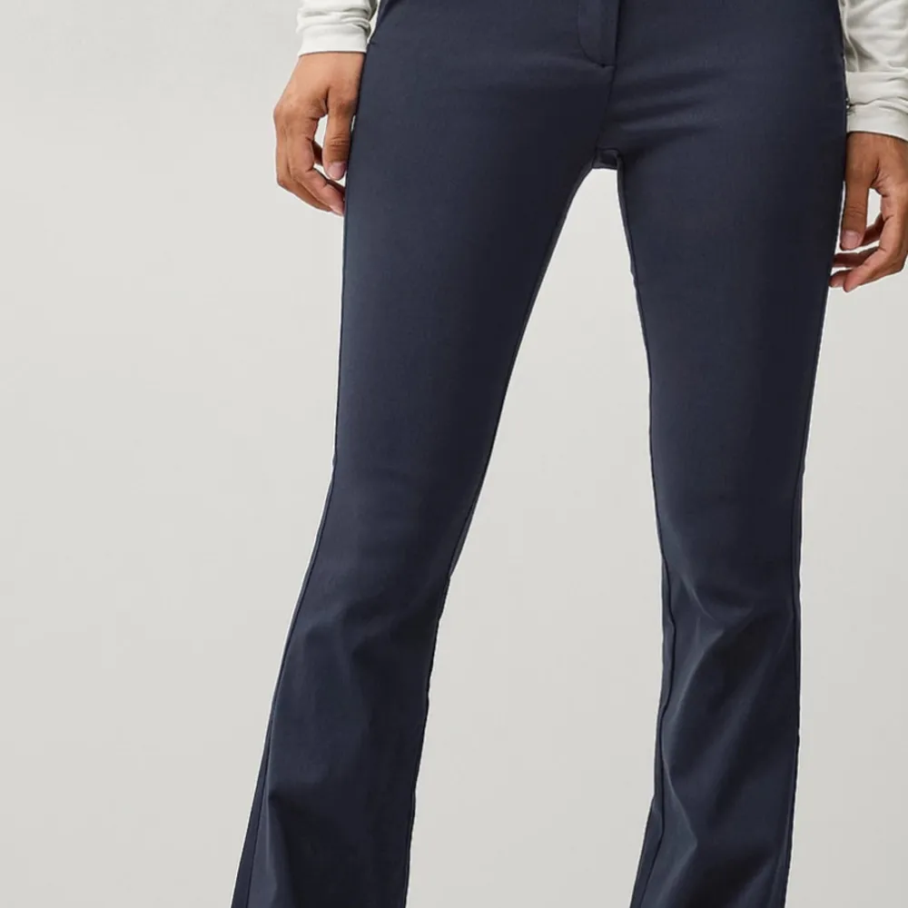 Snygga mörkblå bootcut byxor med låg midja. Perfekta för en stilren look. Byxorna har en klassisk design med dragkedja och knapp framtill.. Farkut & Housut.