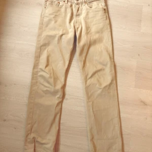 Beige Levis 501 jeans - Säljer ett par klassiska beige Levis 501 jeans. De har en rak passform och är tillverkade i bomull. Byxorna har knappar i gylfen och den ikoniska Levis-lappen baktill.