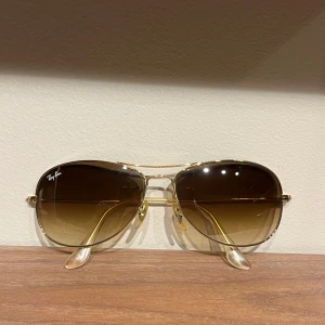 Ray-Ban Brillor - Snygga solglasögon från Ray-Ban med guldfärgad metallram och bruna tonade glas. Perfekt för en stilren look. Den heter Cockpit RB 3362 001 59-14 3N och Kommer med ett svart fodral och en grön putsduk. Nypris 1990kr och skicket är som nytt. 