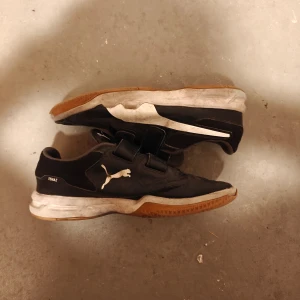 Svarta sneakers från Puma - Säljer ett par svarta sneakers från Puma med vit sula och kardborreband. Skorna har en sportig design med Pumas logga på sidan. Perfekta för en aktiv livsstil.