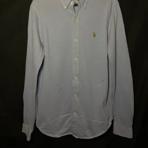 Ralph Lauren skjorta| Ljusblå| Knit Oxford | Stl M - Läs nedan för mer info!😊  Säljer en stilren blå skjorta från Ralph Lauren med klassisk krage och knappar framtill. Skjortan har långa ärmar och ett broderat logotypmärke på bröstet. Perfekt för en snygg och avslappnad look.  Produktinformation:  ✅ Märke: Ralph Lauren  ✅ Storlek: M  ✅ Färg: Ljusblå ✅ Material: Skjorta ✅ Passform: Knit Oxford, stretchigt material ✅ Skick: Mycket bra skick, knappt använd  Frakt och betalning: 📦 Snabb leverans – skickar inom 1-2 dagar efter beställning📦