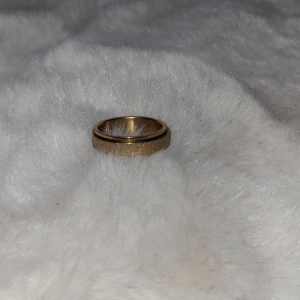 Guldfärgad ring - Det är en snurr ring för stres eller så man inte river på naglarna Elegant guldfärgad ring med en glittrig yta. Ringen har en slät kant som ger en fin kontrast till den glittriga mittdelen. Perfekt för att ge en touch av glamour till din stil. 