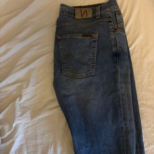 Blå jeans från Nudie Jeans - Snygga blå jeans från Nudie Jeans med klassisk femficksdesign och orange sömmar. De har en normal passform och är tillverkade i slitstarkt denim. Perfekta för en avslappnad stil. Priset ej hugget i sten!