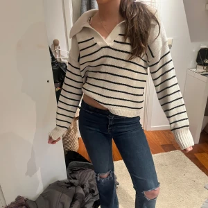 Vit och svart randig tröja - Säljer en snygg vit tröja med svarta ränder och v-ringad krage. Tröjan har långa ärmar och en avslappnad passform som ger en cool look. Perfekt för en casual stil!