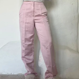 Rosa kostymbyxor - Snygga rosa kostymbyxor med hög midja och rak passform. Byxorna har en stilren design med pressveck framtill och diskreta fickor bak. Perfekta för en chic och elegant look.