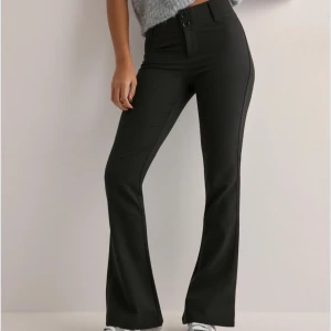 Svarta kostymbyxor med bootcut - Snygga svarta kostymbyxor med bootcut. Byxorna har knappar fram och bakfickor med lock. Perfekta för en stilren look.