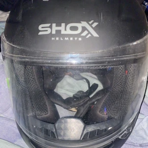 Svart hjälm från Shox - Säljer en svart motorcykelhjälm från Shox med visir. Hjälmen har en stilren design och är perfekt för motorcykelentusiaster. Den är utrustad med vadderad insida för extra komfort. Behöver bara tvättas lite på visyren