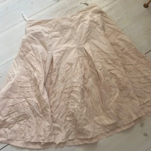 Ljusrosa kjol från Sandwich - Säljer en ljusrosa kjol från Sandwich med vidd och dekorativa sömmar som skapar ett subtilt mönster. Kjolen har veck framtill och är tillverkad i ett mjukt, tunt material som ger ett luftigt intryck.