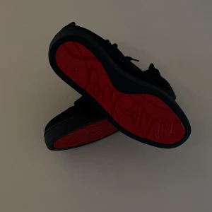 Mörkblåa Loubs🙏 - Säljer ett par svarta sneakers från Christian Louboutin med den ikoniska röda sulan. Skorna har snörning och en stilren design i svart mocka. Perfekta för dig som vill sticka ut med exklusiva detaljer. Hör av er✌️
